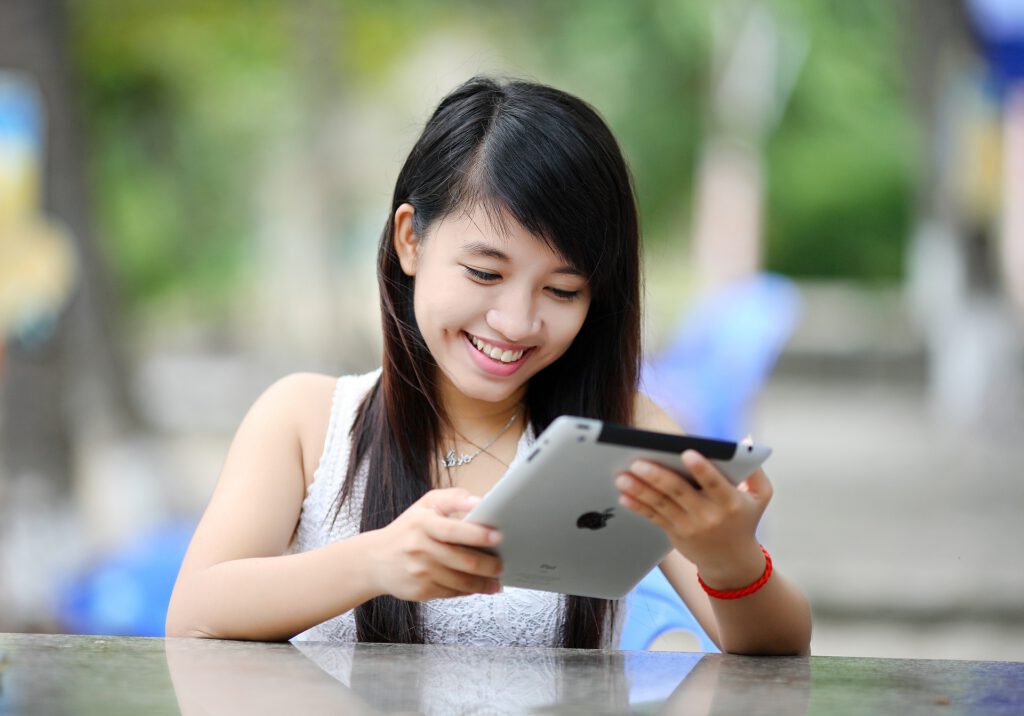 Girl sitting down and smiling at an Ipad during a teletherapy session.