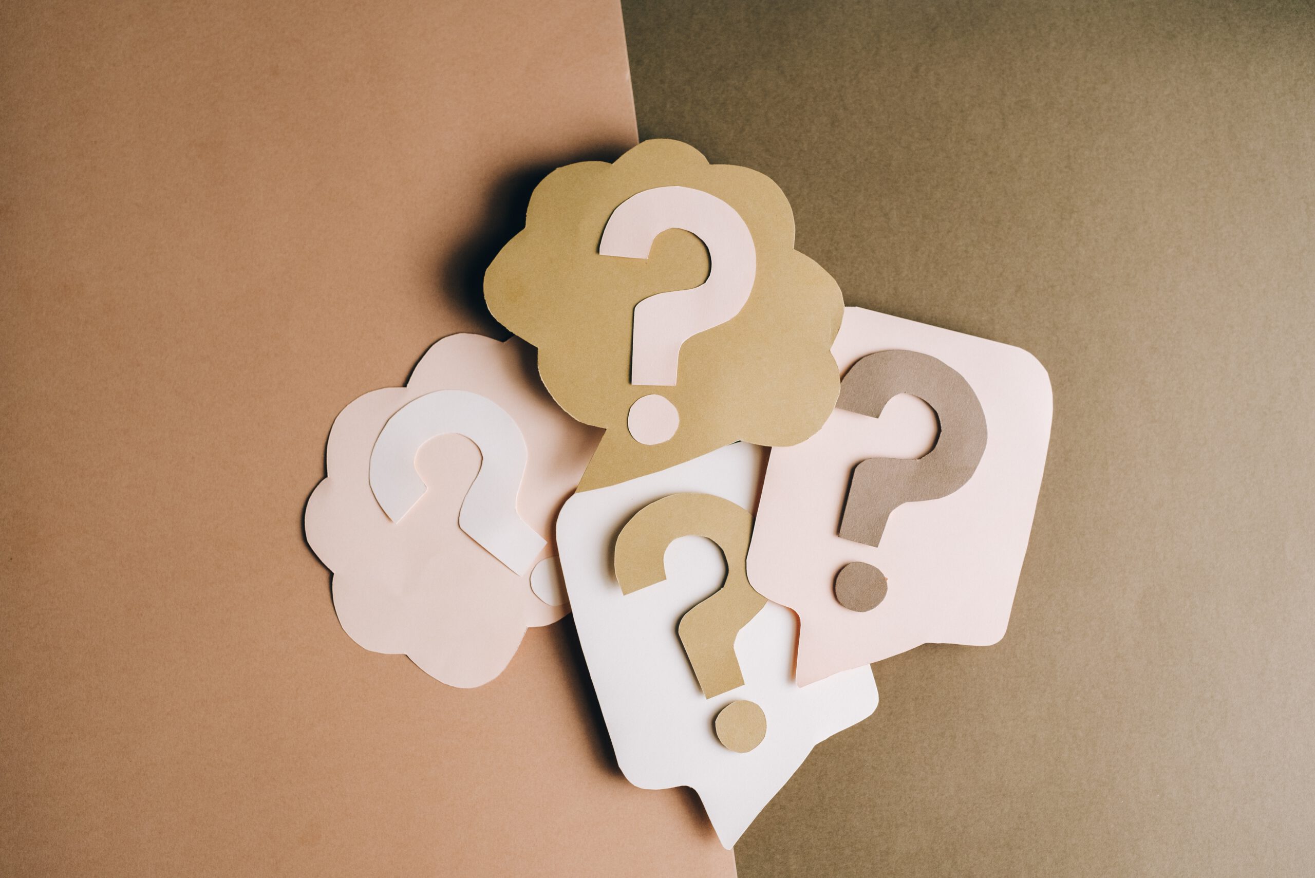 Paper cut-outs of question marks and thought bubbles on a brown paper background.